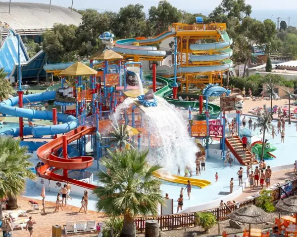 Vaste parc aquatique dans le sud de la France, avec de nombreux toboggans colorés, des jeux d'eau et des palmiers. Ambiance festive et familiale.