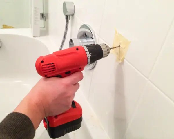 Main tenant utilise une perceuse pour percer du carrelage mural dans une salle de bain.