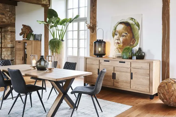Salle à manger style industriel avec table en bois, chaises grises, buffet en chêne et tableau d'enfant.