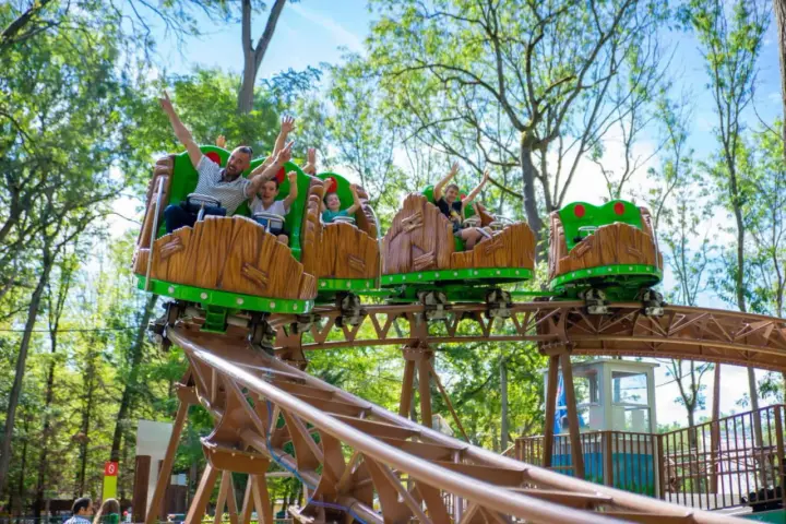 Famille joyeuse sur des wagons de montagnes russes en bois dans un parc attraction ile de france.