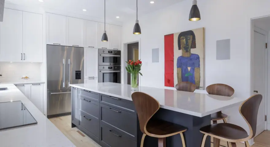 Cuisine moderne avec îlot central gris, comptoirs en quartz, armoires blanches et tableau abstrait. Idées pour comment rénover sa cuisine.