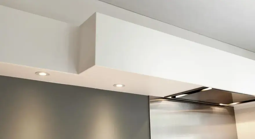 Éclairage discret sous un faux plafond de cuisine moderne, intégrant une hotte aspirante en inox.