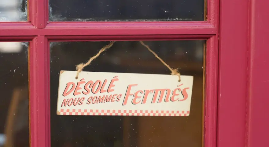 Panneau "Désolé, nous sommes fermés" sur une porte rouge. Il est donc probable que ce commerce ne soit pas ouvert le 1er mai.