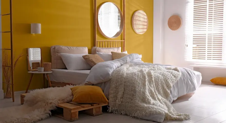 Une chambre d'adulte lumineuse avec un mur jaune soleil, un lit douillet et une décoration murale en rotin.