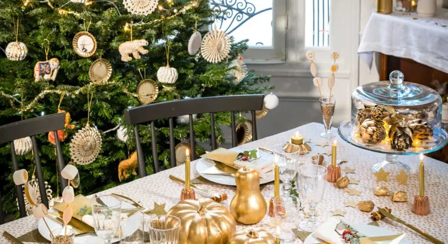 Déco table de Noël pas cher à faire soi-même : sapin décoré, citrouilles dorées, guirlandes lumineuses et vaisselle festive créent une ambiance chaleureuse.