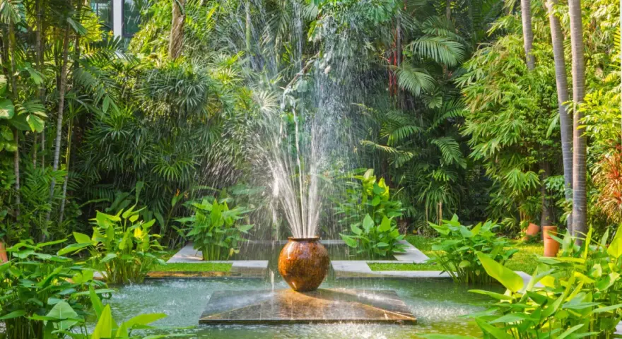 Fontaine d'eau jaillissant d'un pot en terre cuite, au cœur d'un jardin luxuriant. Une **original déco jardin récupération** qui invite à la détente.