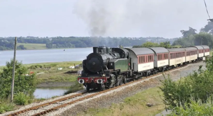 Le petit train du Trieux, avec ses tarifs attractifs, traverse un paysage verdoyant longeant une étendue d'eau.