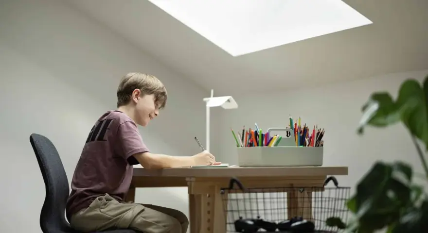 Un jeune garçon dessine joyeusement à son bureau sous pente, éclairé par une grande fenêtre de toit.