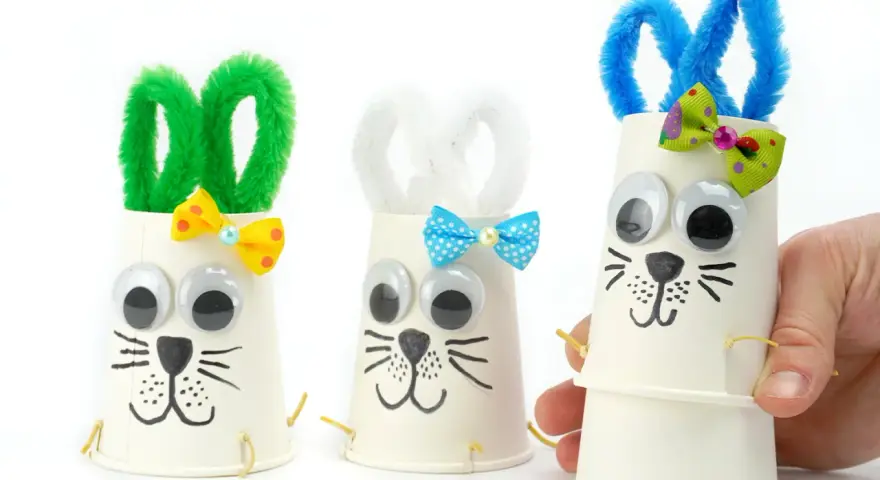 Trois adorables lapins de Pâques bricolage faits avec des gobelets en papier, des pompons et des yeux mobiles. Parfait pour une activité de Pâques !