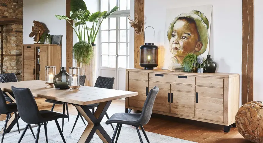 Salle à manger style industriel avec table en bois, chaises grises, buffet en chêne et tableau d'enfant.