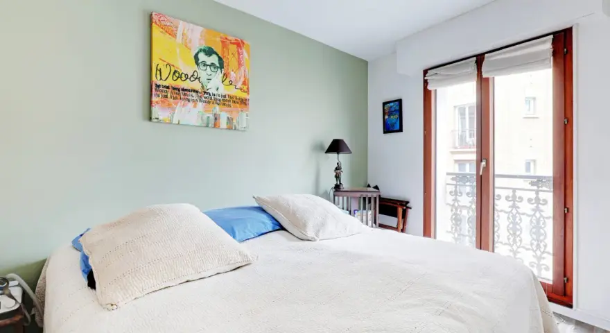 Chambre avec un mur vert pastel, un lit blanc et une œuvre d'art de Woody Allen. On dirait qu'ils ont décidé de peindre 2 murs sur 4.