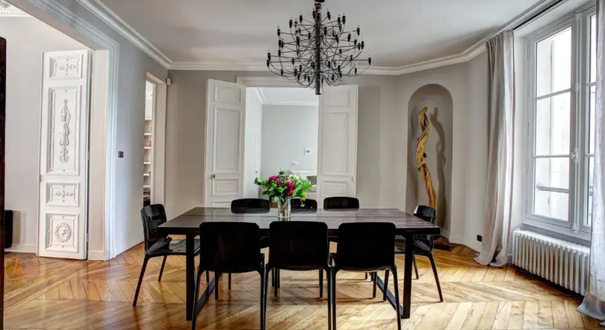 Salle à manger élégante dans un type de maison haussmannien, avec parquet ancien, lustre moderne et bouquet de fleurs.