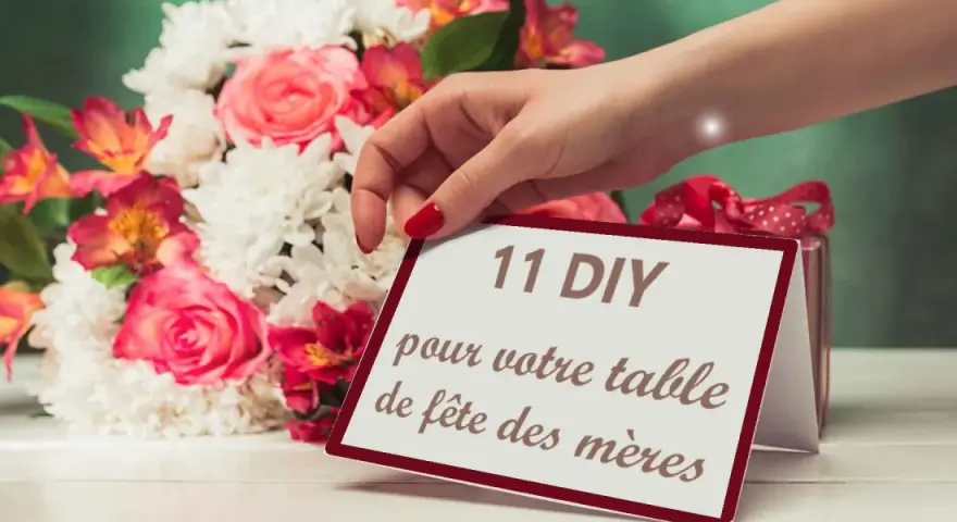 Une main dépose une carte "11 DIY pour votre table de fête des mères" près d'un bouquet de fleurs roses et blanches.