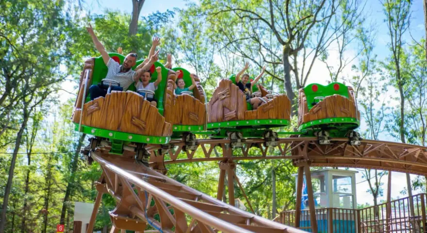 Famille joyeuse sur des wagons de montagnes russes en bois dans un parc attraction ile de france.