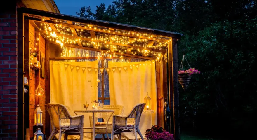 Une terrasse accueillante illuminée par des guirlandes lumineuses, une belle idée éclairage terrasse pour des soirées magiques. Meubles en rotin et fleurs ajoutent à l'ambiance.