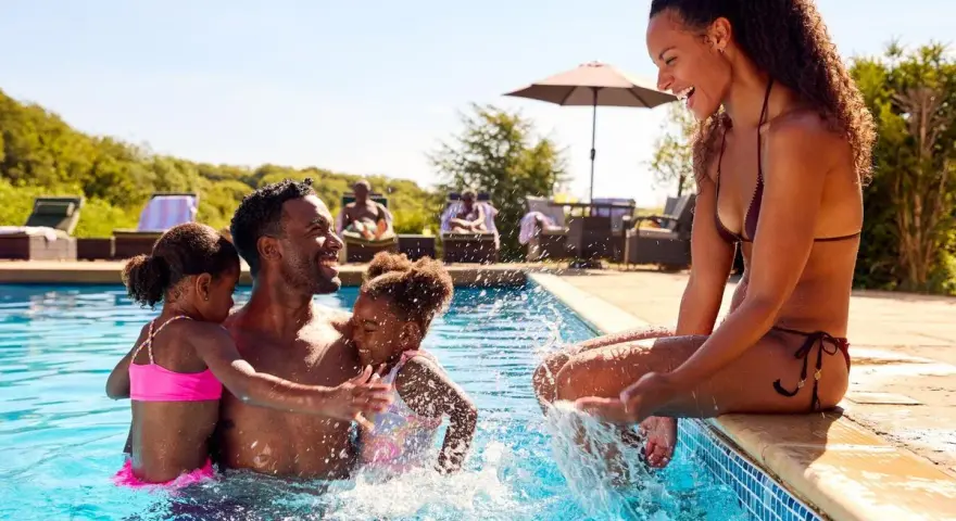 Famille s'amusant dans une piscine, un père avec ses deux filles, une mère assise au bord. Le cadre parfait pour le meilleur center parc France.