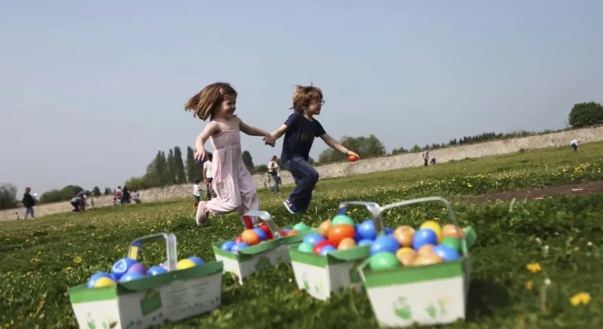 Deux enfants courent joyeusement dans un champ fleuri, leurs paniers remplis d'œufs colorés, signe d'une joyeuse chasse aux œufs.