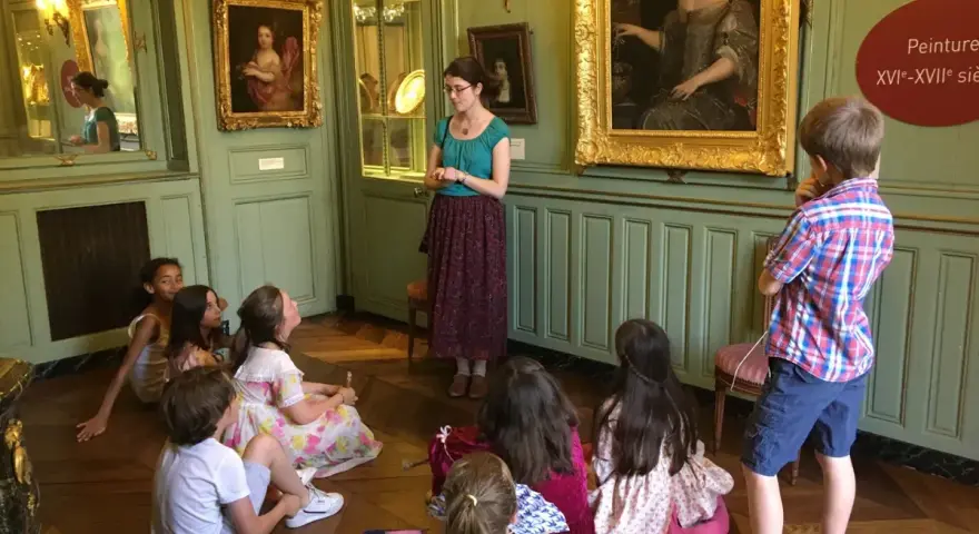 Visite guidée d'un musée dans les Yvelines : des enfants écoutent attentivement une guide devant des tableaux.