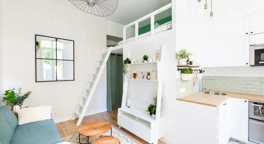 Aménagement intérieur appartement optimisé avec mezzanine, canapé bleu, étagères et coin cuisine moderne.