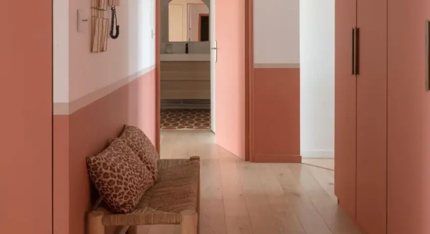 Banc en rotin avec coussins léopard, murs bicolores corail et blanc, portes roses. Une belle idée déco couloir moderne.