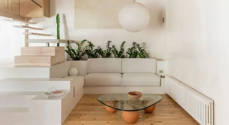 Salon au style wabi sabi, avec un canapé blanc, une table basse en verre et bois, des plantes vertes et un escalier en bois brut.