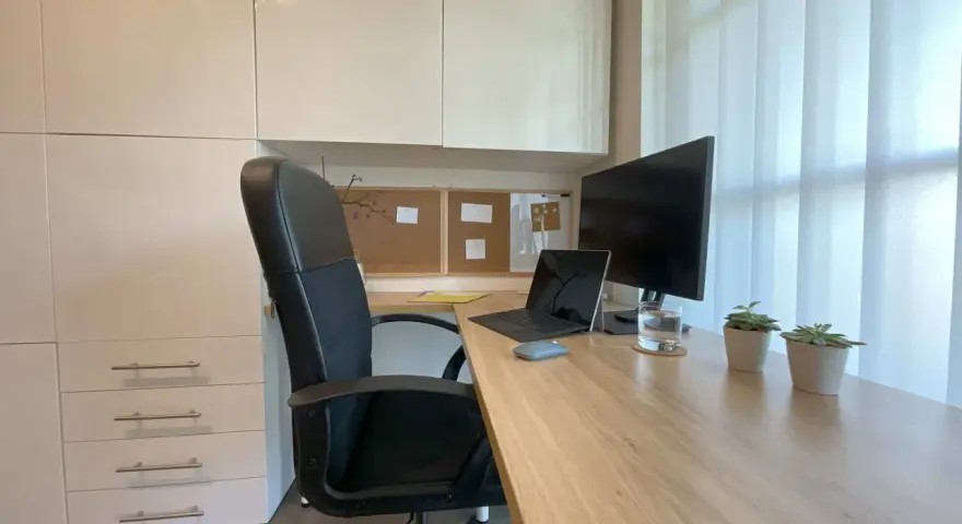 Bureau moderne avec fauteuil noir, bureau en bois clair, ordinateur portable, écran, plantes et stores blancs. Une belle idee deco bureau pour un espace fonctionnel et apaisant.