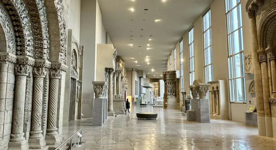 Vaste galerie de la Cité de l'architecture et du patrimoine, présentant des éléments architecturaux romans et gothiques, avec des colonnes sculptées et des arcs en plein cintre.