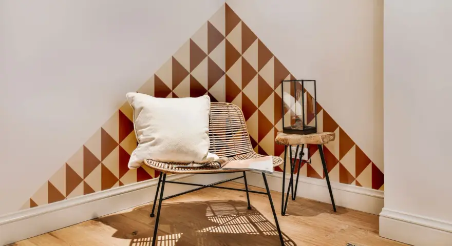 Un coin cosy avec un fauteuil en rotin, un coussin blanc et un motif géométrique sur le mur. Une belle idée motif peinture mur pour un style unique.