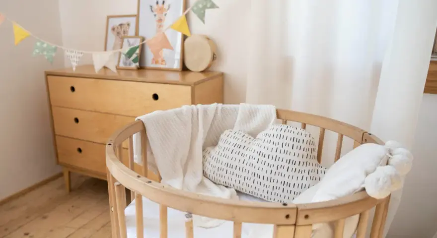 Aménagement chambre enfant : berceau en bois, coussin nuage, plaid douillet et commode vintage. Guirlande de fanions joyeuse.