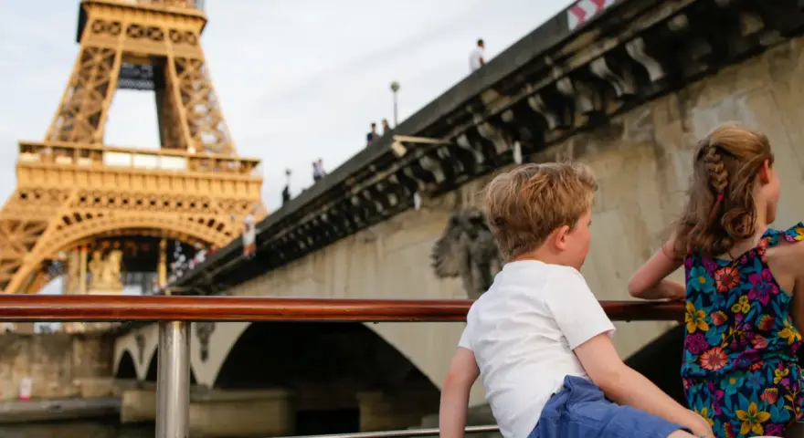 Deux enfants profitent d'une croisière sur la Seine à Paris la nuit, avec la Tour Eiffel illuminée en arrière-plan.