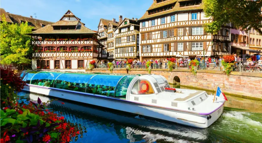 Bateau touristique naviguant sur un canal à la Petite France à Strasbourg, avec ses maisons à colombages et ses balcons fleuris.