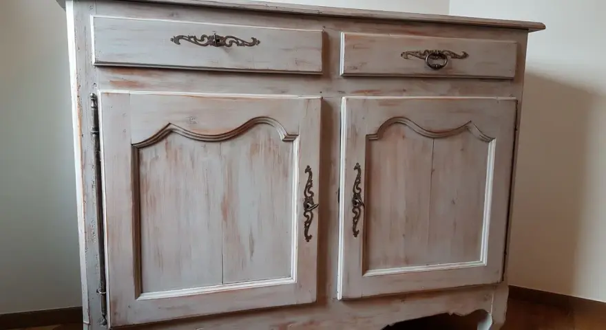 Buffet ancien patiné, avec deux tiroirs et deux portes ornées de poignées en bronze. Le bois présente une finition usée pour un style vintage.