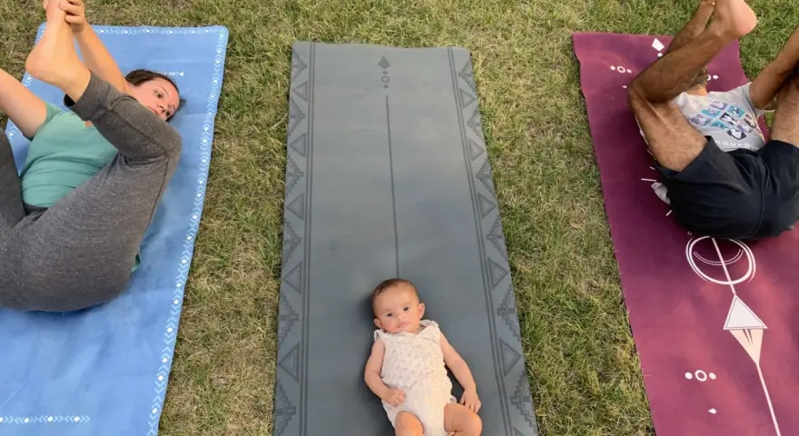 Un bébé sur un tapis de yoga, entouré de ses parents pratiquant le yoga. Une séance de yoga pour enfants en plein air.