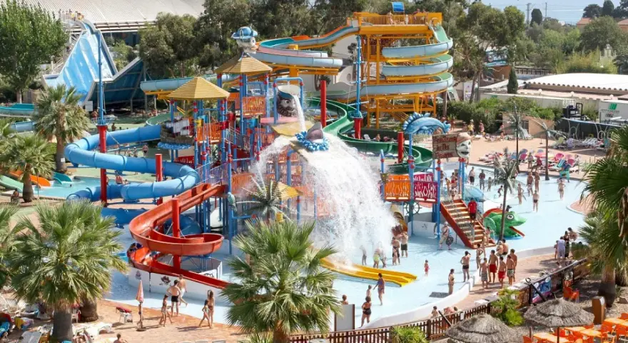 Vaste parc aquatique dans le sud de la France, avec de nombreux toboggans colorés, des jeux d'eau et des palmiers. Ambiance festive et familiale.