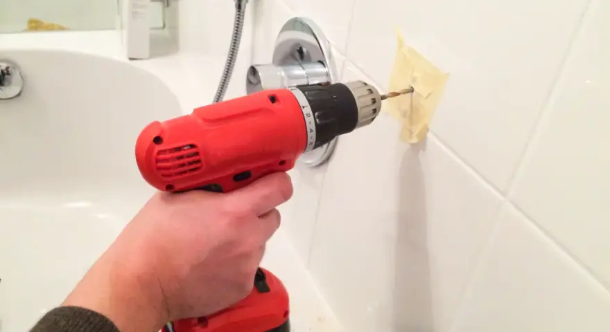 Main tenant utilise une perceuse pour percer du carrelage mural dans une salle de bain.
