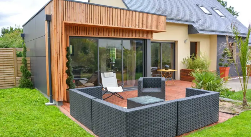 Agrandissement maison ossature bois avec terrasse moderne et mobilier extérieur.
