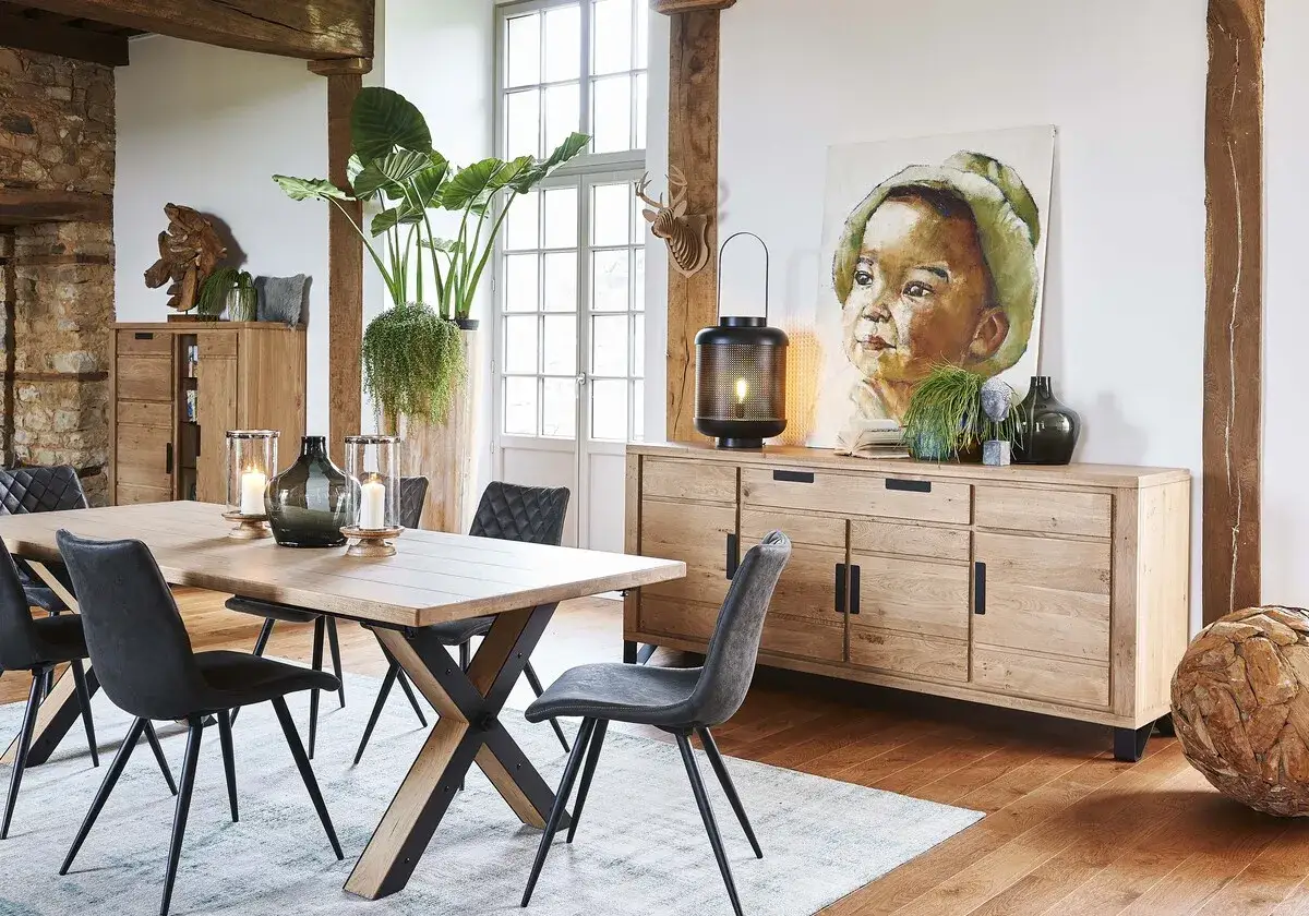 Salle à manger style industriel avec table en bois, chaises grises, buffet en chêne et tableau d'enfant.