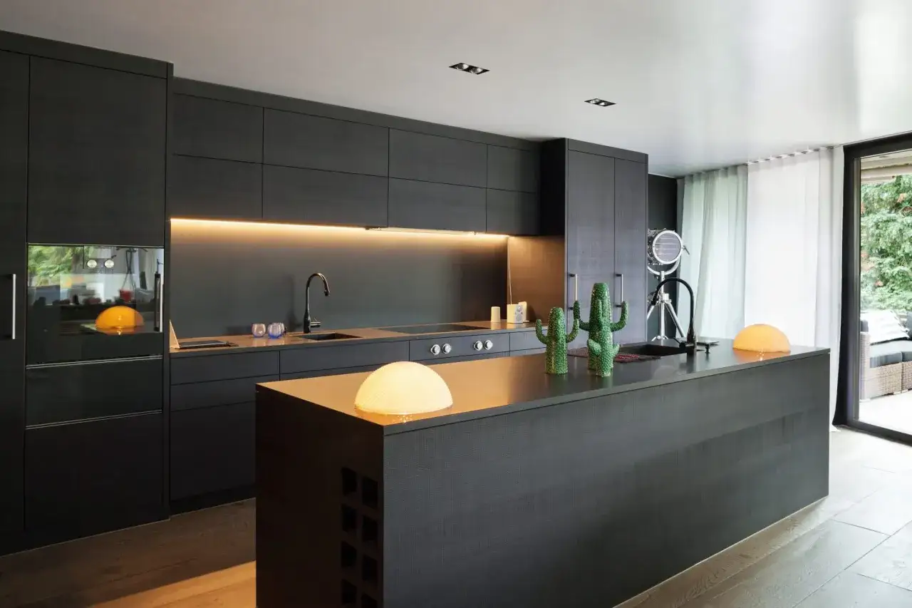 Cuisine moderne, résultat d'une rénovation appartement avant après. Meubles sombres, îlot central, éclairage d'ambiance et cactus décoratifs.