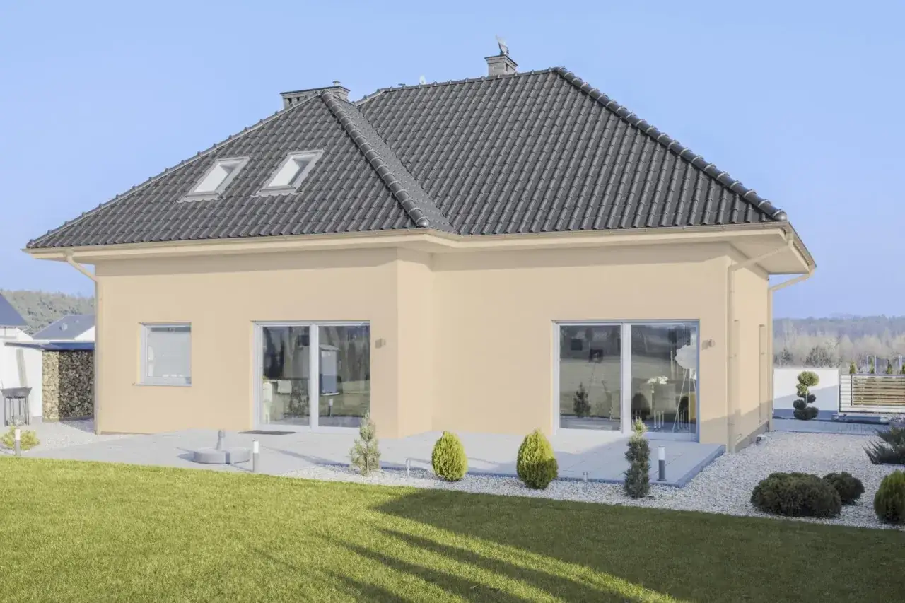 Maison moderne avec une couleur de façade maison tendance beige clair, toit sombre, grandes fenêtres et jardin verdoyant.