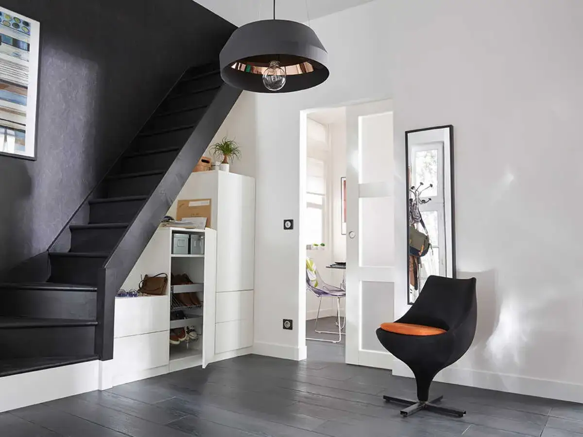 Un vestibule moderne, idéal pour une maison feng shui, avec un escalier noir, des rangements blancs et un fauteuil design.