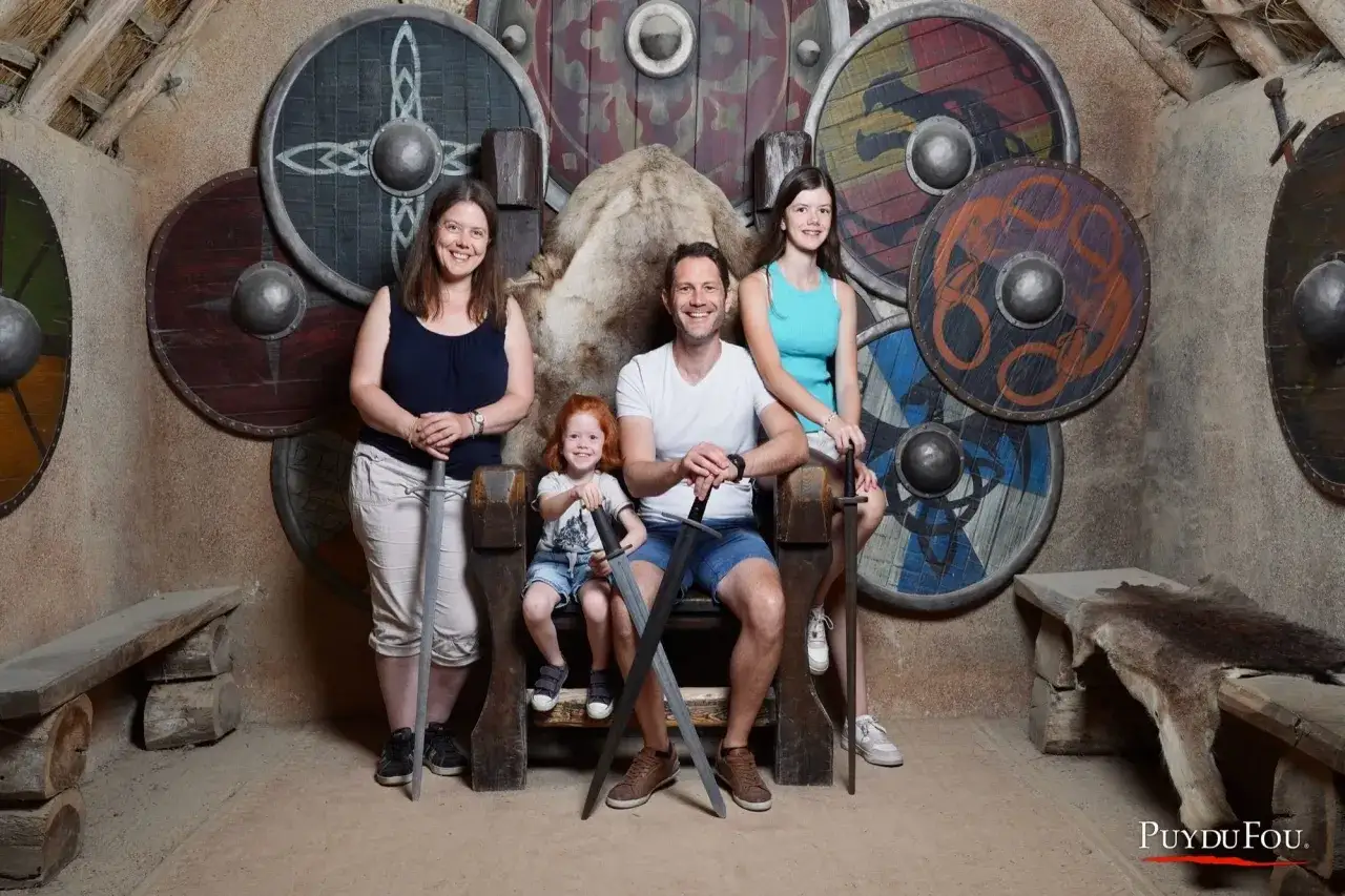 Une famille pose devant des boucliers vikings au Puy du Fou, un souvenir m&eacute;morable pour tous les &acirc;ges.