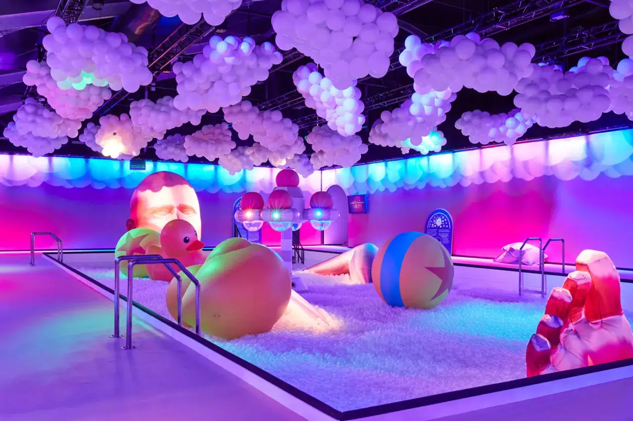Un monde onirique &agrave; Paris : une piscine &agrave; balles g&eacute;ante sous des nuages de ballons, avec des jouets iconiques et une t&ecirc;te monumentale.