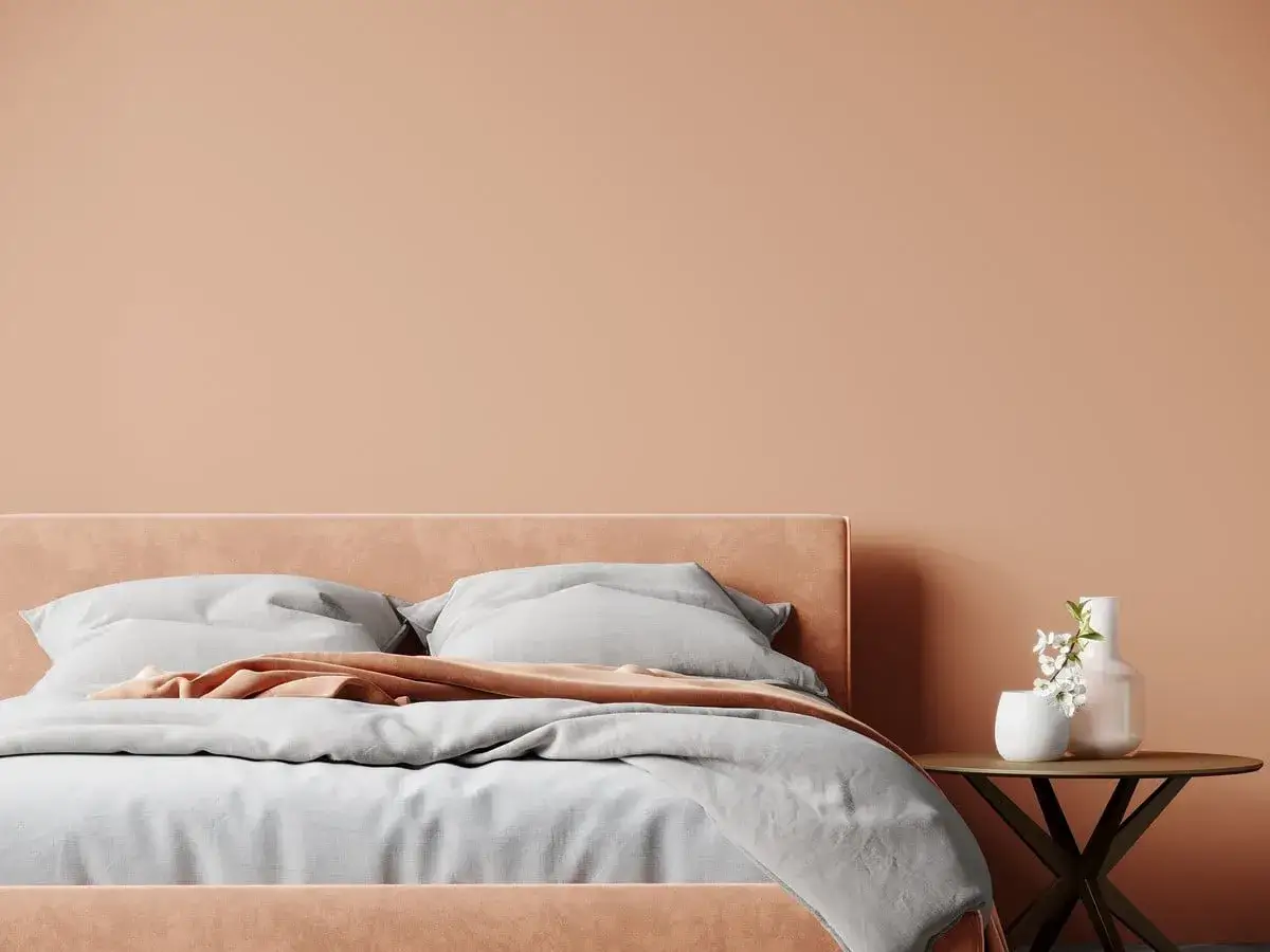 Une chambre adulte apaisante avec un lit douillet et une peinture murale couleur pêche. Un petit bout de table avec des vases fleuris complète l'ambiance.