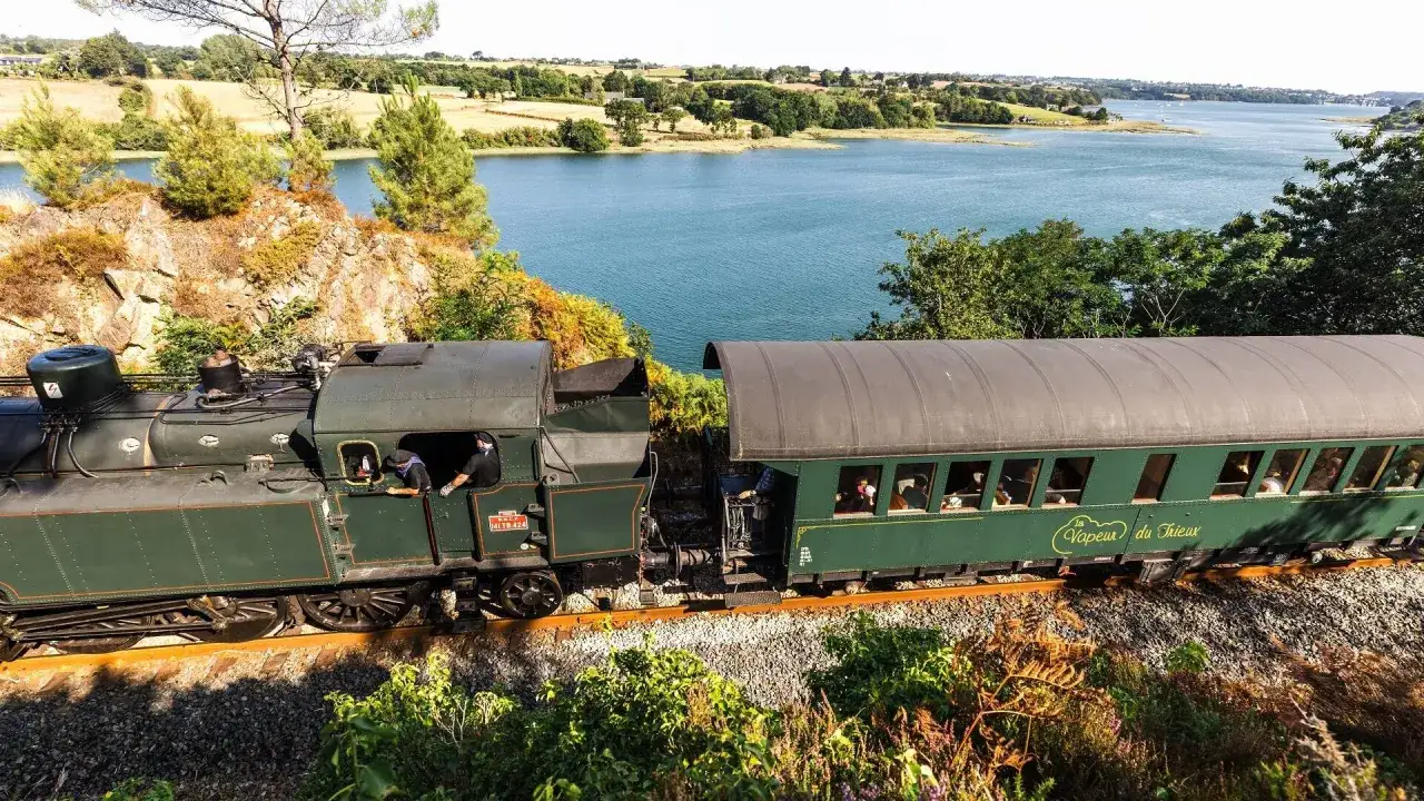 Le petit train du Trieux, avec ses tarifs attractifs, traverse un paysage pittoresque au bord d'un lac bleu.