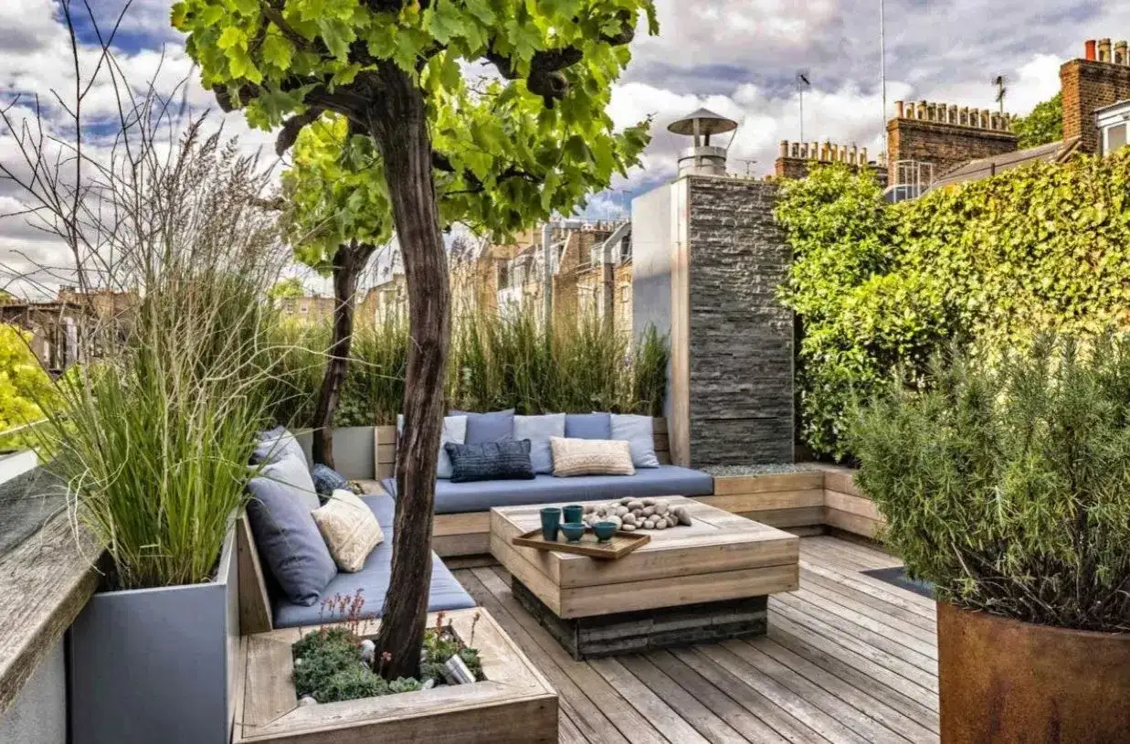 Un coin salon confortable sur l'une des plus belles terrasses en bois, avec des coussins bleus, une table basse en bois et une végétation luxuriante.
