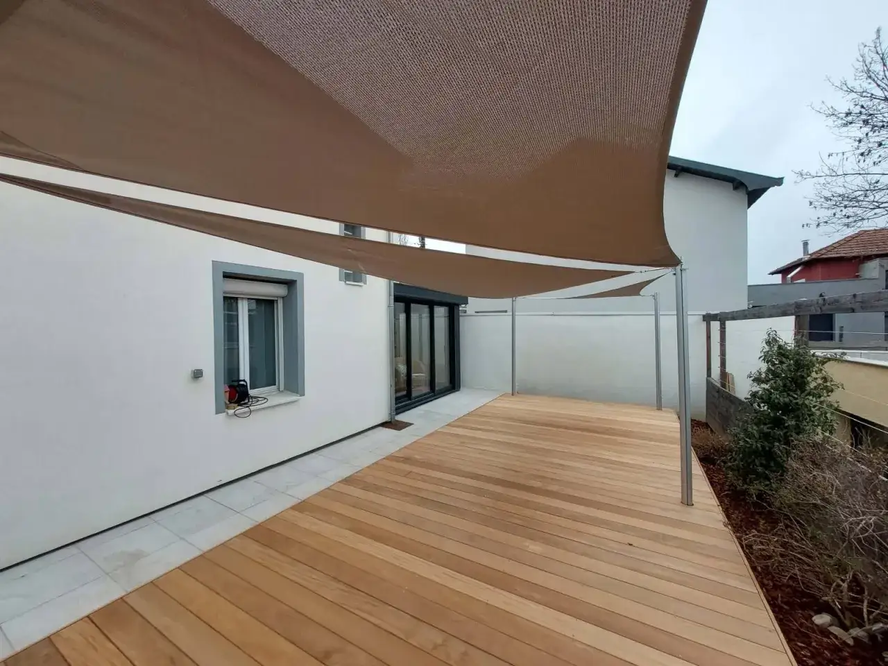 Une terrasse sur pilotis moderne en bois avec un voile d'ombrage brun, offrant un espace ext&eacute;rieur &eacute;l&eacute;gant et fonctionnel.