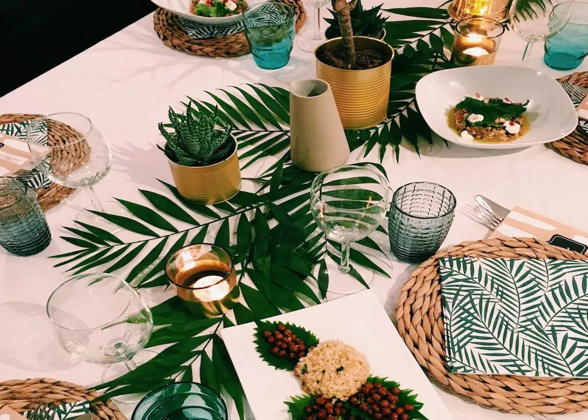 Idées de décoration de table tropicale : feuilles de palmier, plantes en pot, bougies et vaisselle élégante créent une ambiance festive.
