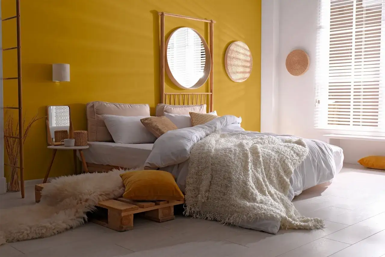Chambre cosy avec mur jaune vif et blanc. Le lit est par&eacute; de draps blancs et d'une couverture textur&eacute;e. Le jaune et le blanc sont 2 couleurs qui vont bien ensemble pour une chambre.