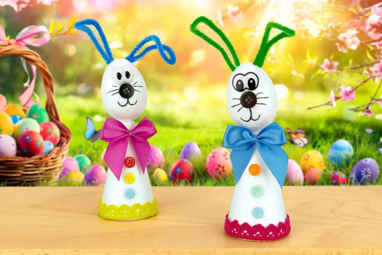 Deux adorables lapins de Pâques bricolage, faits maison, avec des oreilles en chenille et des nœuds colorés, posent devant un panier d'œufs de Pâques.