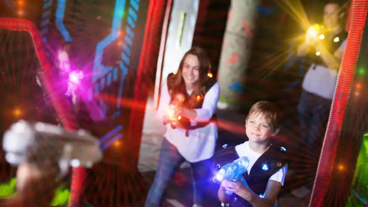 Un garçon et une femme souriants jouent au laser game, une super activité enfant à Reims.